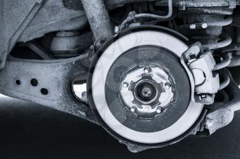 Shiny brake disk and suspension spring. Replacing wheel on SUV car. Close-up blue toned photo
