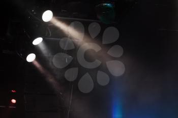 Three spot lights with strong beams in smoke over dark background, modern stage illumination equipment