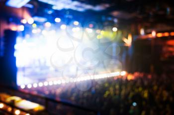 Blurred photo background, life music concert stage with colorful illumination and crowd of people