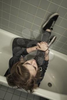Sad teenage girl in dark clothes sitting in empty bath. Depression mood concept. Vintage tonal correction photo filter