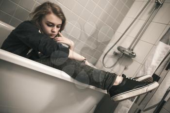 Stressed sad European teenage girl sitting in bath. Depression mood concept. Vintage tonal correction dark photo filter