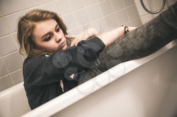 Stressed sad European teenage girl sitting in bath. Depression mood concept. Vintage tonal correction photo filter