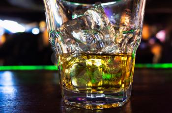 Glass of whiskey with ice stands on the bar. Close-up photo with soft selective focus