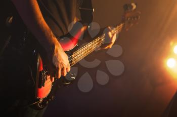 Guitarist plays on of bass guitar in scenic lights, soft selective focus, live music theme