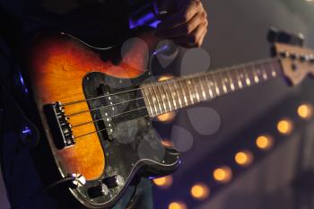 Close-up photo of bass guitar in guitarist hands, soft selective focus, live rock music theme