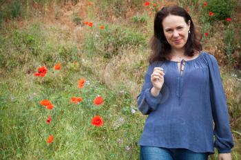 Smiling young adult European woman walks on a summer meadow with flowering poppies. Outdoor portrait
