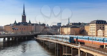 Cityscape of Gamla Stan city district in central Stockholm with blue subway train going on bridge