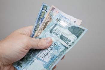 Male hand holding Jordanian dinars banknotes over gray background