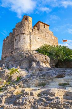 Medieval stone castle and flag of Catalonia on the rock in Spain. Main landmark of Calafell town, vertical photo