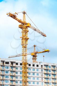Yellow cranes work in modern concrete living houses massive under construction
