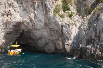 Small recreation motorboat enters the grotto in coastal rocks of Capri island, Italy
