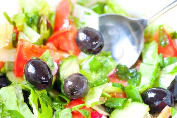 Closeup photo of fresh side dish with salad, tomatoes, olives, cucumbers and a metal spoon