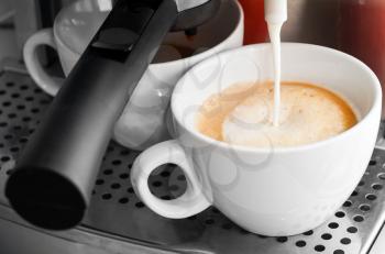Coffee maker pouring hot milk in white cup to prepare cappuccino