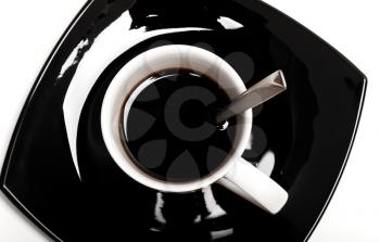 Coffee in white cup with spoon on black saucer,  top view isolated on white