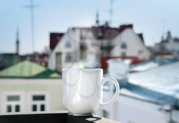 White cup stands on balcony railing above blurred cityscape