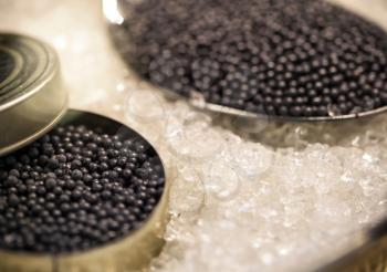 Macro with black caviar in small round metal tin and spoon on ice