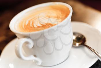 Cappuccino coffee with spice and artistic foam in a white cup