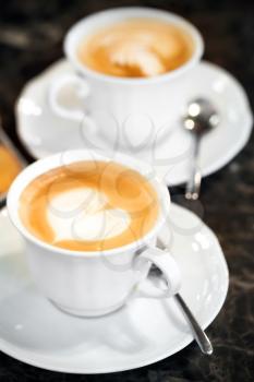 Two white cups of Cappuccino with heart shaped milk foam. Selective focus