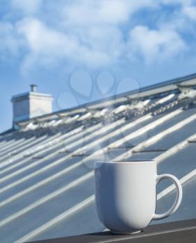 White cup stands on balcony railing with roof on a background