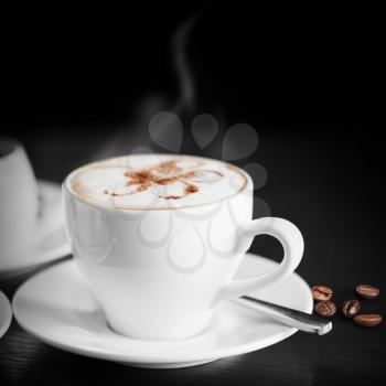 White cup of hot cappuccino on black background