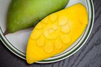 Yellow mango in white plate on black wooden table