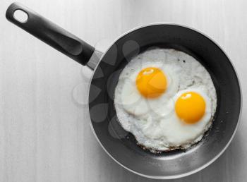 Two scrambled eggs in black frying pan on white wooden table