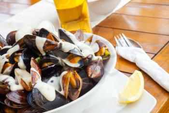 Plate full of mussels with garlic sauce on wooden table in restaurant 