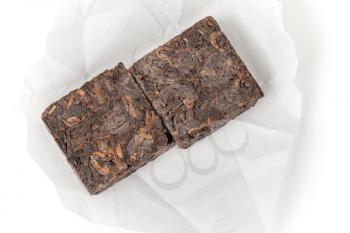 Small pressing briquette of black Chinese Shu Pu-erh tea in paper on white background