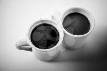 Two cups full of coffee stand on a table with black shadow, monochrome stylized photo