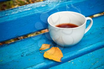 White cup of black tea is on old blue wooden bench in autumn park.  Selective focus with shallow DOF, vintage tonal photo filter, retro style photo