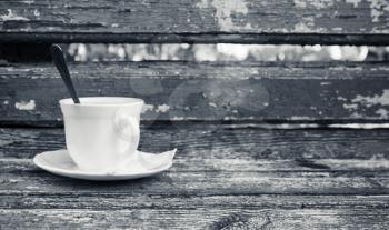 Cup of coffee is on old wooden bench in autumn park.  Selective focus with shallow DOF, monochrome photo