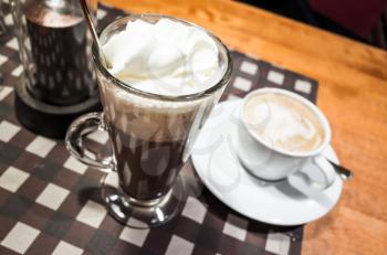 Glass of hot chocolate and white cup of cappuccino coffee stand on a table 