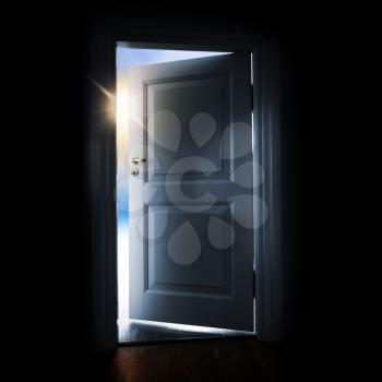 Opening blue door in a dark room with shining light and sky outside