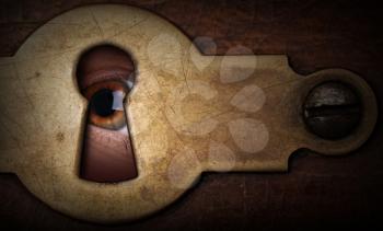Brown eye looking through a vintage metal keyhole