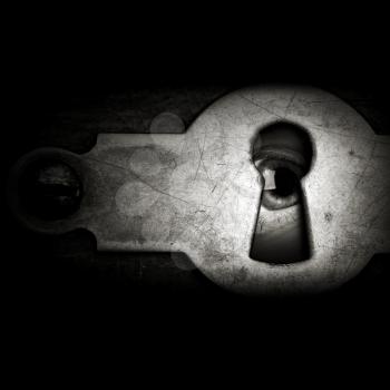 Eye looking through a vintage metal keyhole in the dark