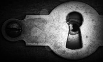 Eye looking through an old dark metal keyhole
