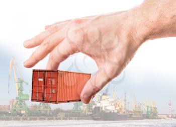 Bright red metal freight shipping container in man's hand above port background