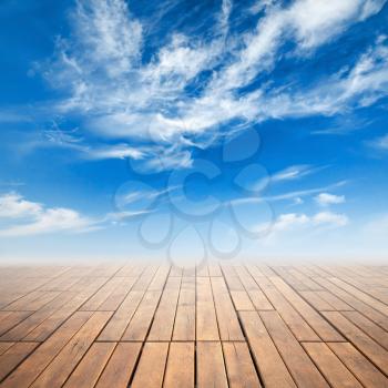 Brown wooden floor with perspective and bright cloudy sky