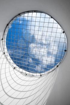 Abstract empty white interior fragment. Blue cloudy sky behind the round window with metal grid