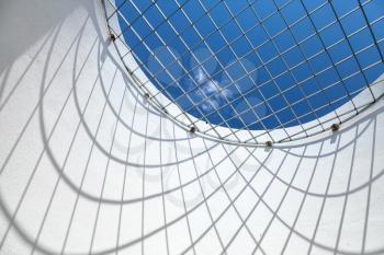 Abstract white interior fragment. Blue sky behind the round window with metal grid