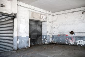 Abstract empty white interior of old automotive garage with asphalt pavement and closed metal gates