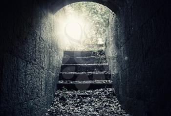 Glowing exit with stairs and lens flare from dark abandoned concrete tunnel interior, tonal correction filter