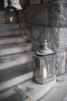 Old metal outdoor lamps with burning candles stands on stone stairs