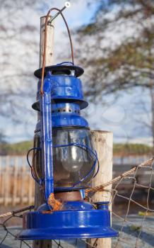 Blue vintage kerosene lamp hangs on old outdoor fence
