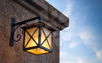 Ancient street lamp mounted on stone wall over blue sky background