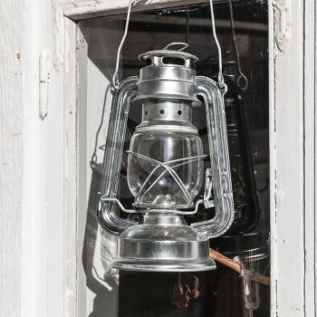 Shining metal kerosene lamp hangs on white wooden frame in Finland