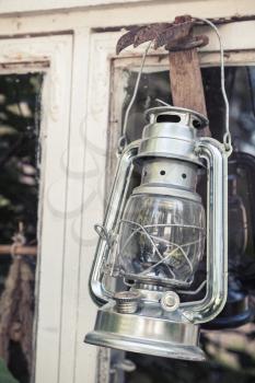 Shining metal kerosene lamp hangs on white wooden frame in Finland, vintage toned photo with old style filter effect