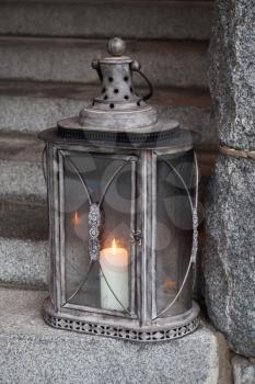 Old metal outdoor lamp with burning candle stands on stone stairs