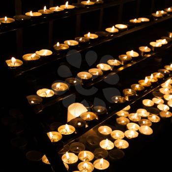 Small candles burning on shelves in dark catholic church