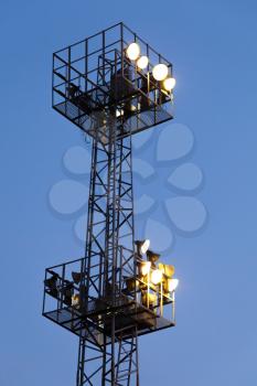 Industrial light mast with glowing lamps on dark blue sky background